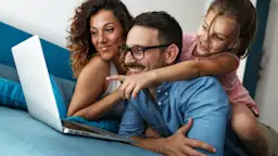 Günstige Tarife bei der NEW Energie Eine Familie sitzt zusammen auf dem Sofa und schaut sich die Tarife der NEW Energie an. Ein Mädchen zeigt aufgeregt auf den Laptop.