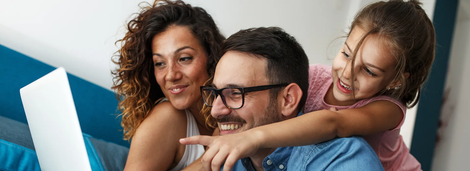 Günstige Tarife bei der NEW Energie Eine Familie sitzt zusammen auf dem Sofa und schaut sich die Tarife der NEW Energie an. Ein Mädchen zeigt aufgeregt auf den Laptop.