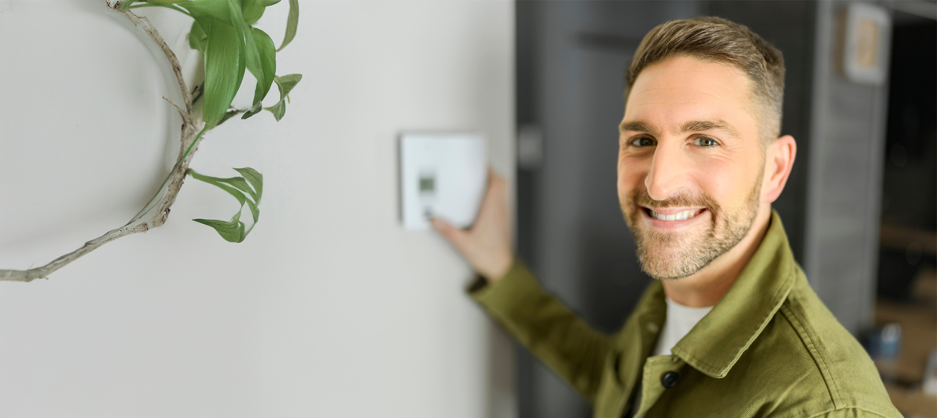 Ein Mann steht lächelnd vor einer Wand, mit der Hand an einem Bedienelement.