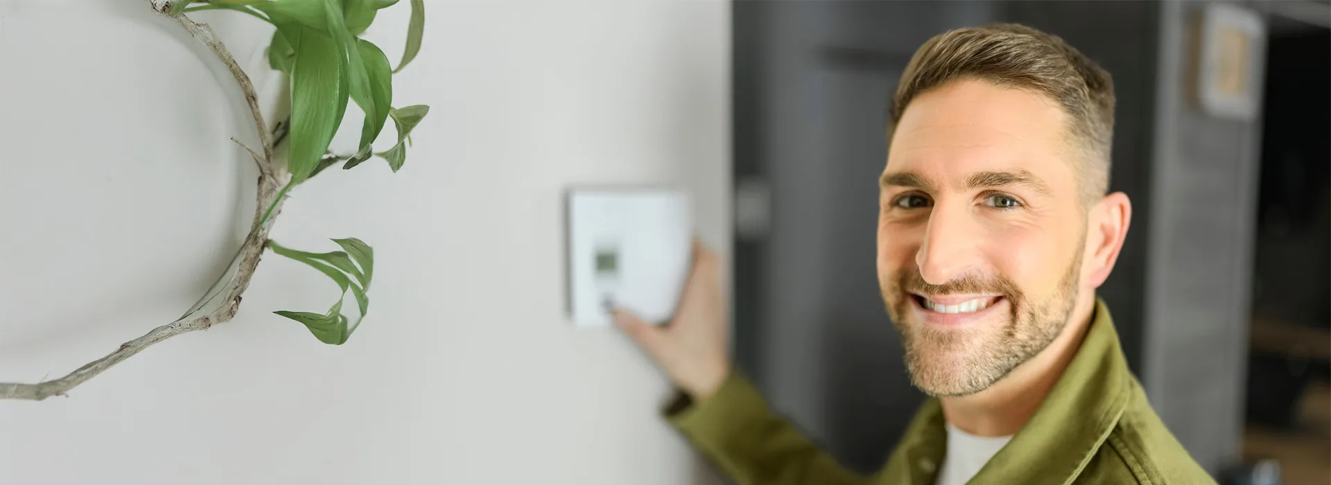 Heizung mieten mit NEW Energie Ein Mann steht lächelnd vor einer Wand, mit der Hand an einem Bedienelement.