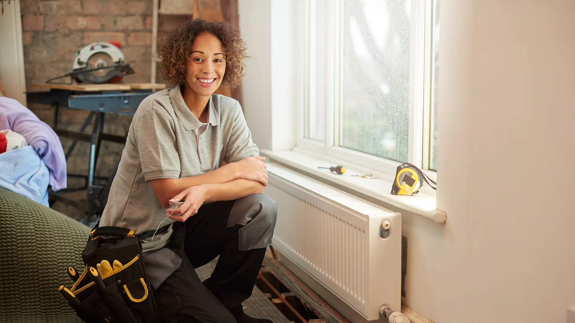 Sichere Wärmeversorgung Eine Handwerkerin kniet vor einer Heizung und kümmert sich um die Wärmeversorgung. Der Heizstrom kommt von der NEW Energie.