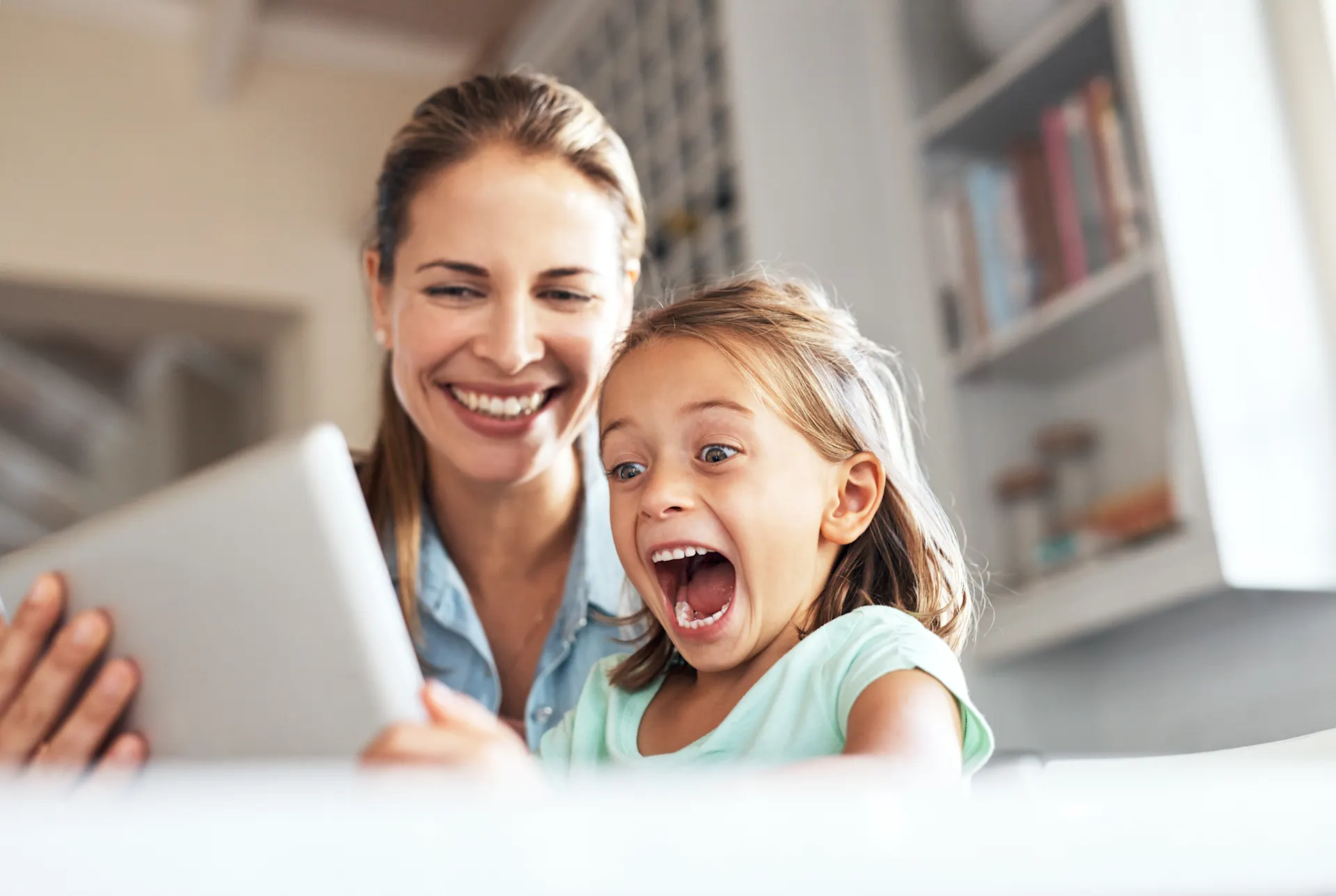 Eine Frau sitzt mit einem Kind vor einem Tablet und sie freuen sich über attraktive Tarife.