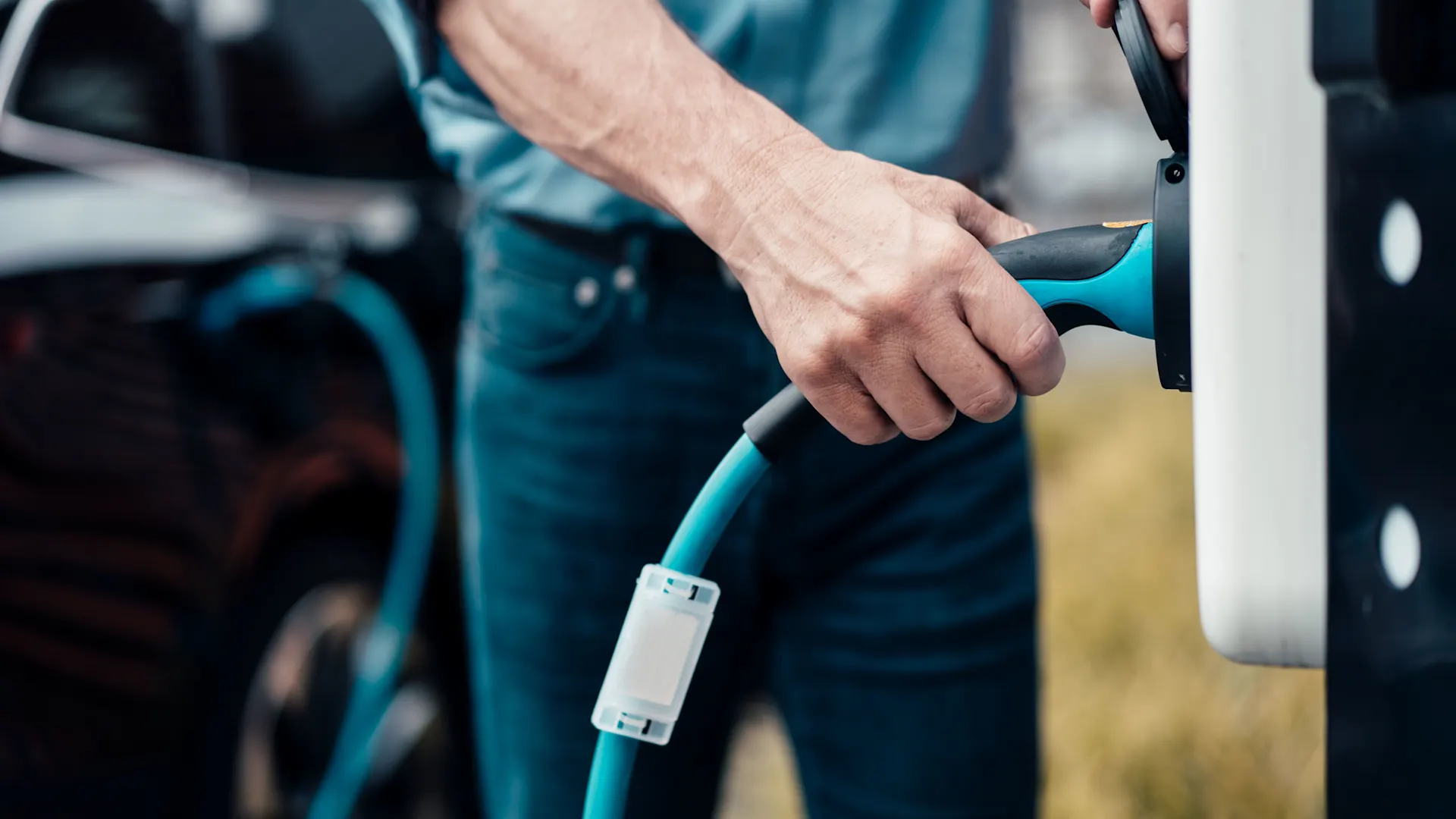 Günstiger Autostrom fließt durch das Ladekabel Das Ladekabel wir von einem Mann in die Wallbox gesteckt und das Auto wird mit günstigem Autostrom geladen.