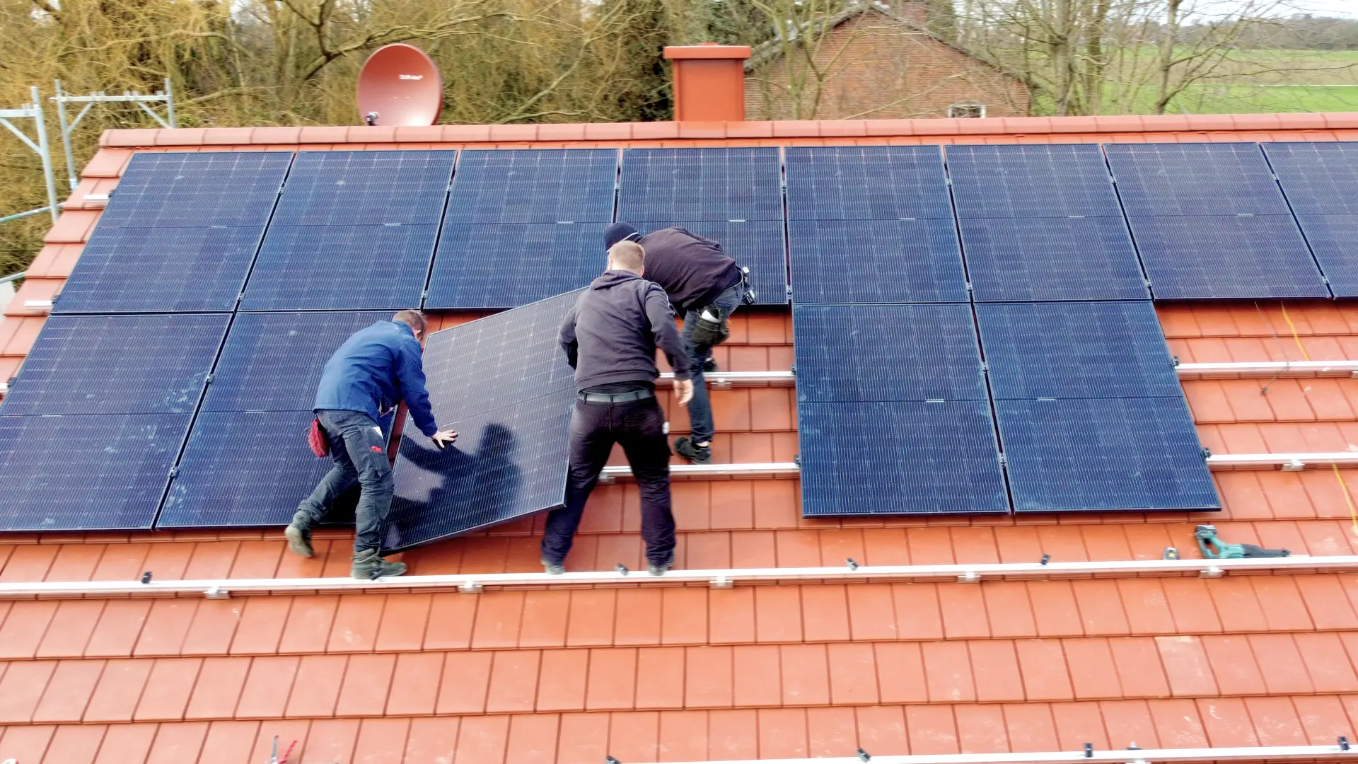 Mehrere Männer montieren eine Photovoltaik Anlage auf einem Dach zur Herstellung von Oekostrom.