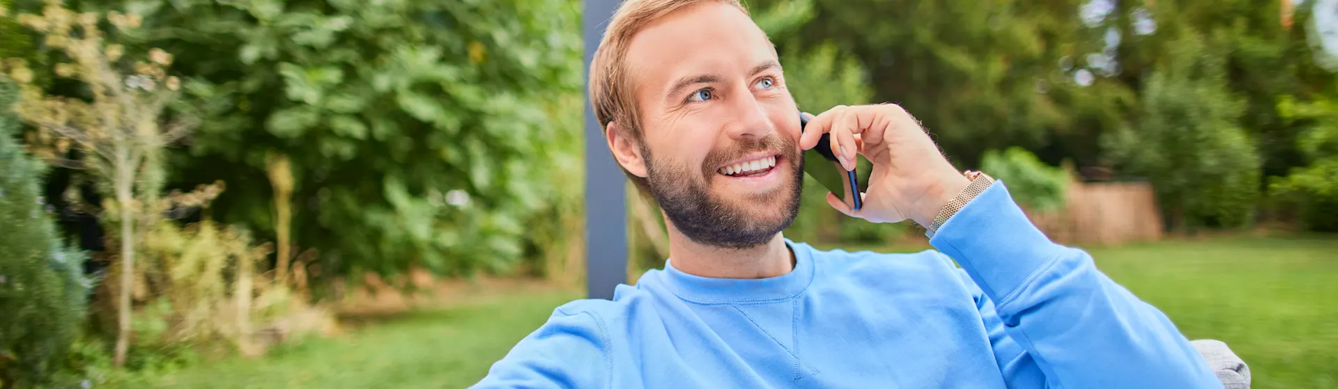 Telefonischer Kundenservice Ein Mann sitzt mit einem Smartphone auf einem Sofa im Garten und nutzt den telefonischen Kundenservice der NEW Energie um Strompreise zu vergleichen.