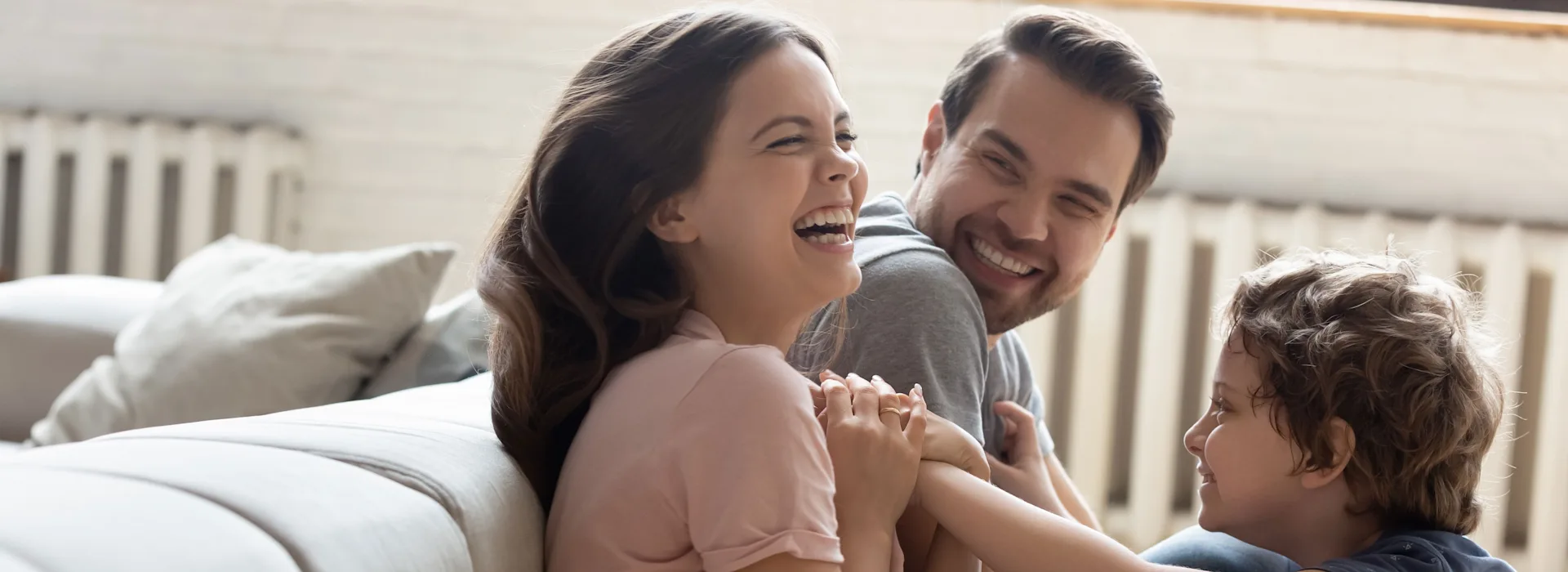 Energie von der NEW Energie - mehr Zeit für wichtigere Dinge Ein Paar sitzt auf dem Boden und spielt mit ihrem Sohn vor einem Sofa.