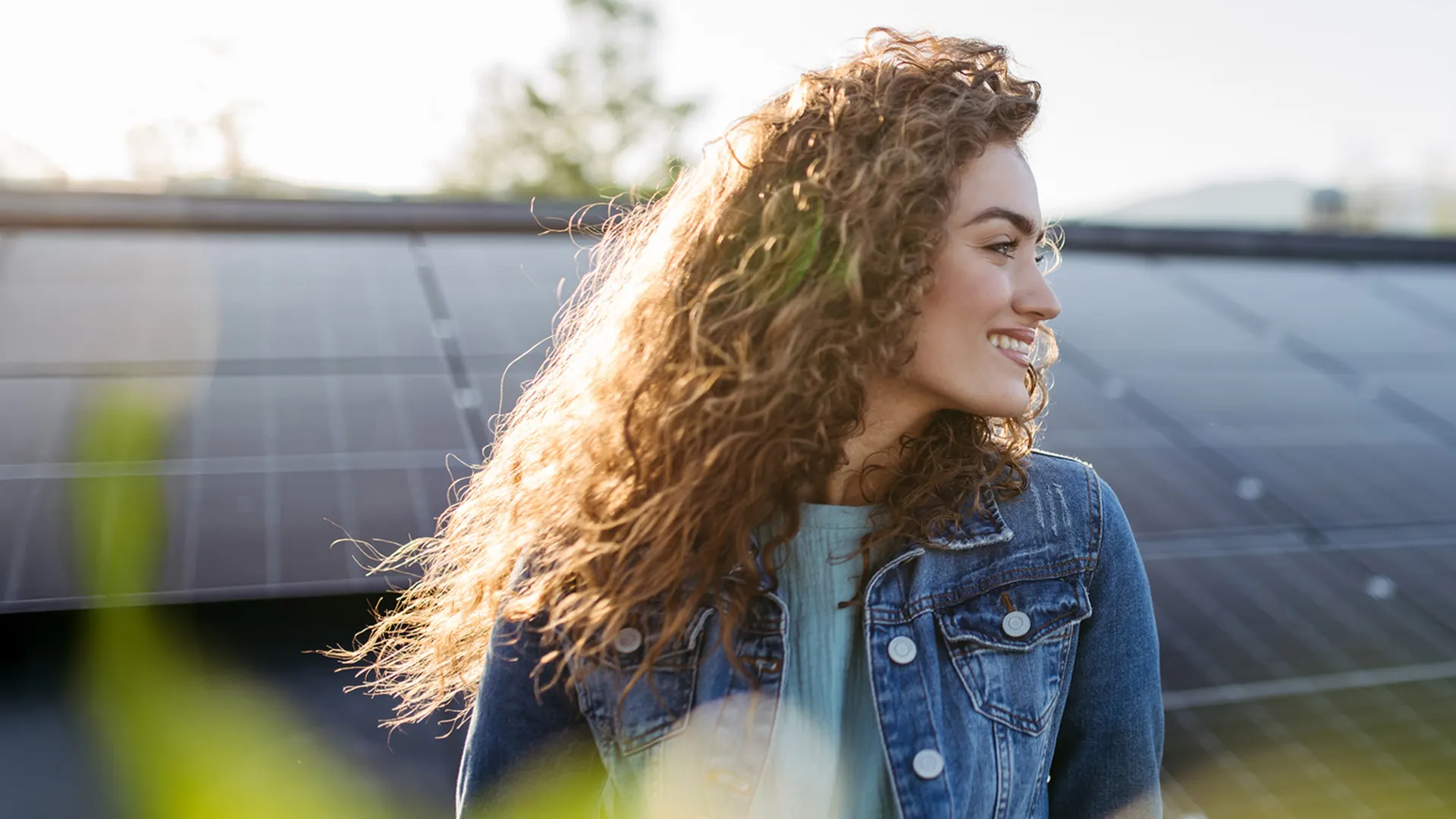 Frau steht lachend vor der NEW Energie Photovoltaik-Anlage Frau sitzt lächelnd vor einer PV-Anlage der NEW Energie und schaut zur Seite.