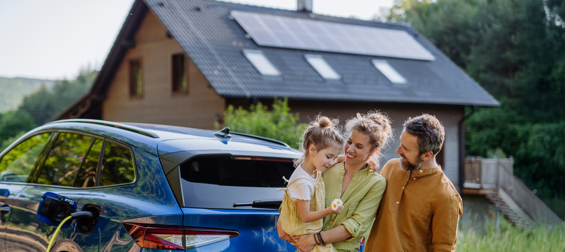 Familie steht vor einem mit Haus im Grünen, mit einer PV-Anlage auf dem Dach und einem Elektroauto davor.