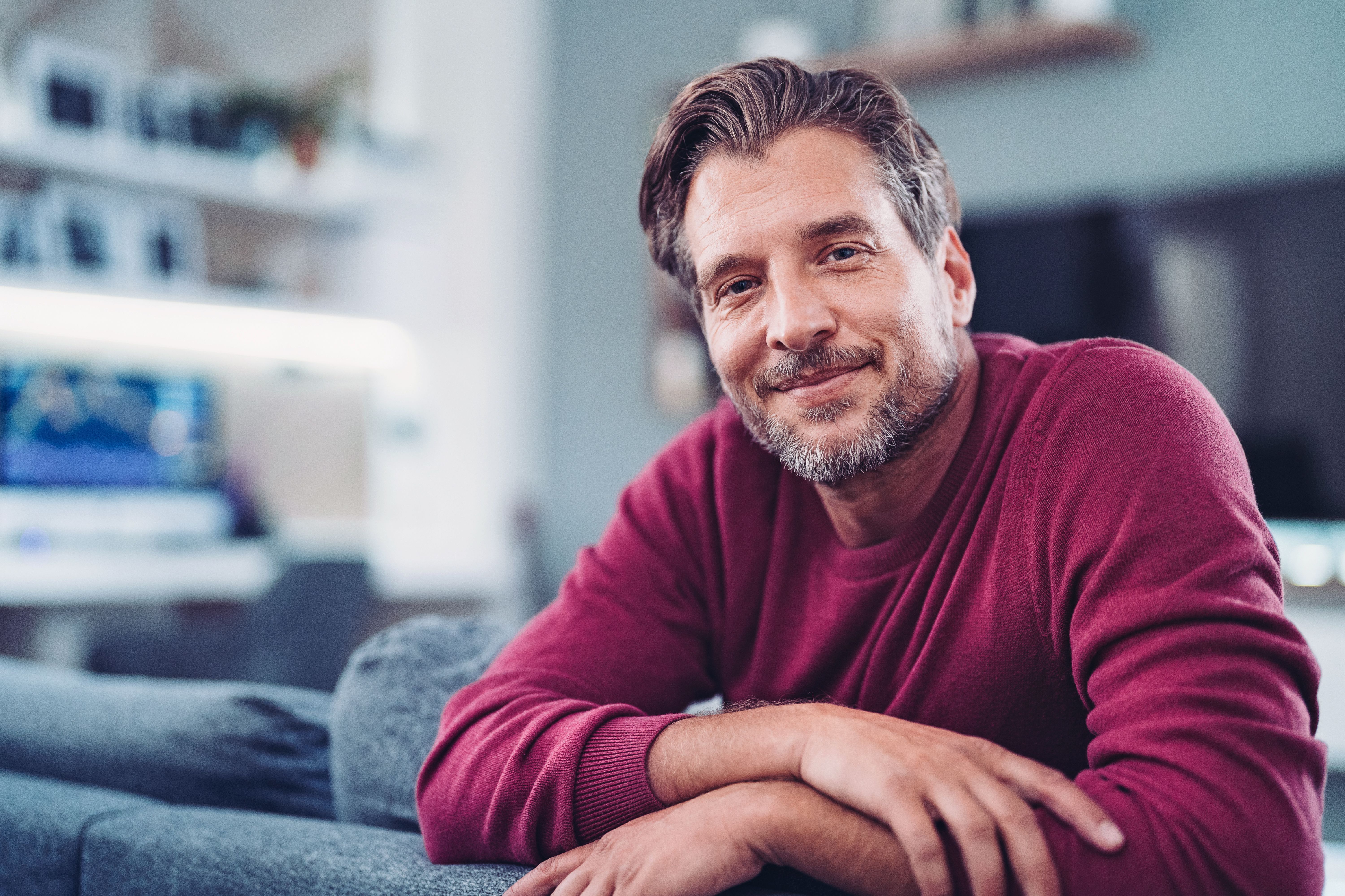 Ein Mann sitzt entspannt auf seiner blauen Couch und schaut über die Rückenlehne. 