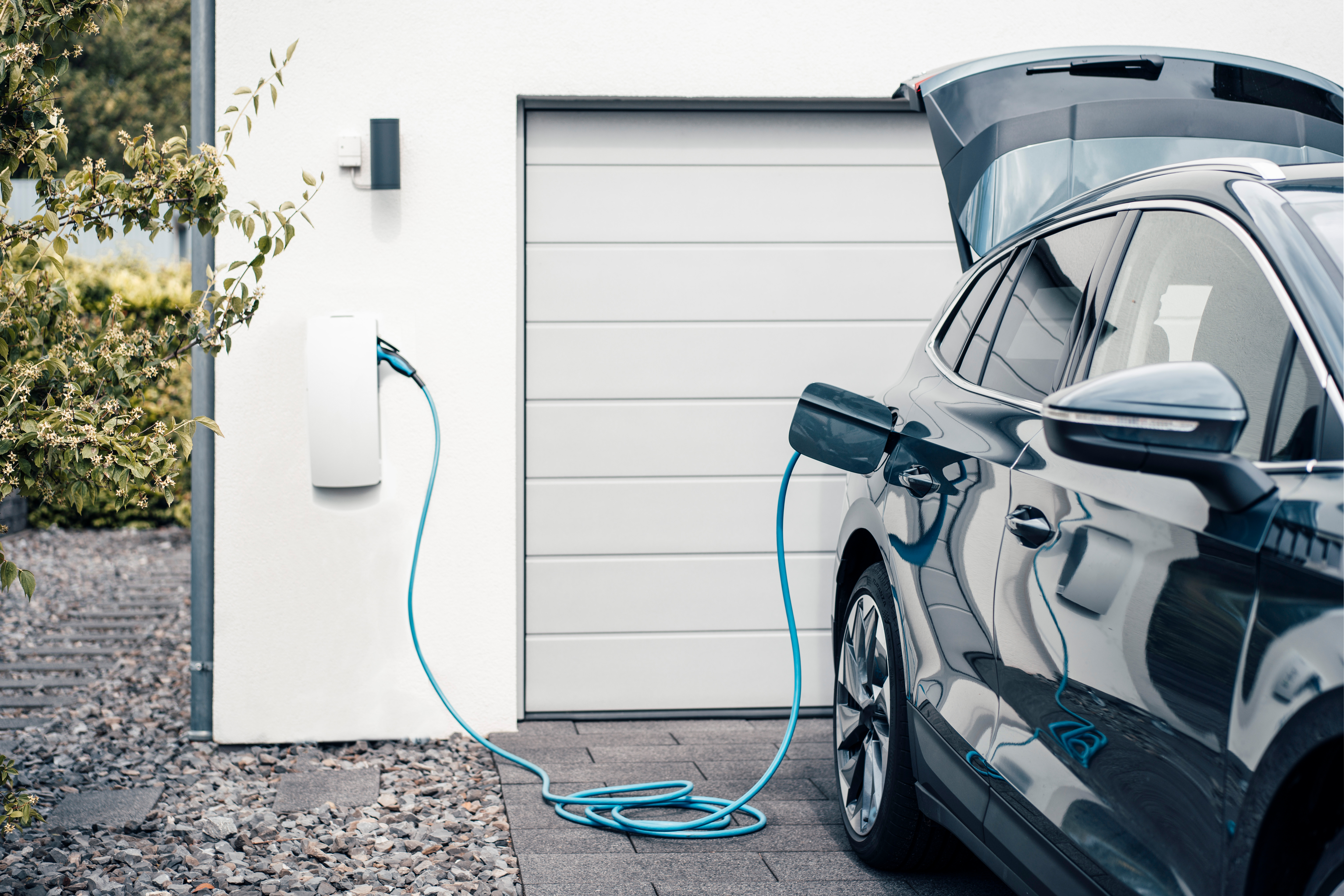 Ein Elektroauto ist an einem Haus an eine Ladestation angeschlossen.