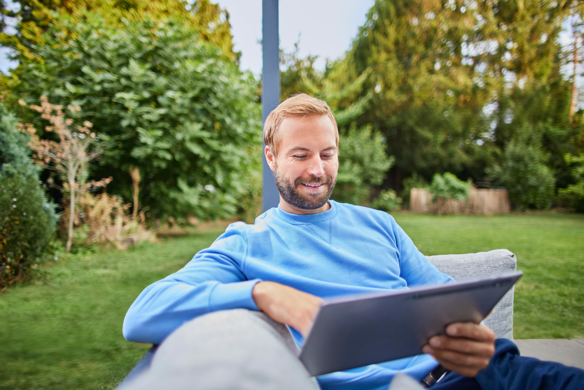 Ein Mann sitzt im Garten mit einem Tablet und ist einen Tarif am berechnen und informiert sich über verschiedene Themen.