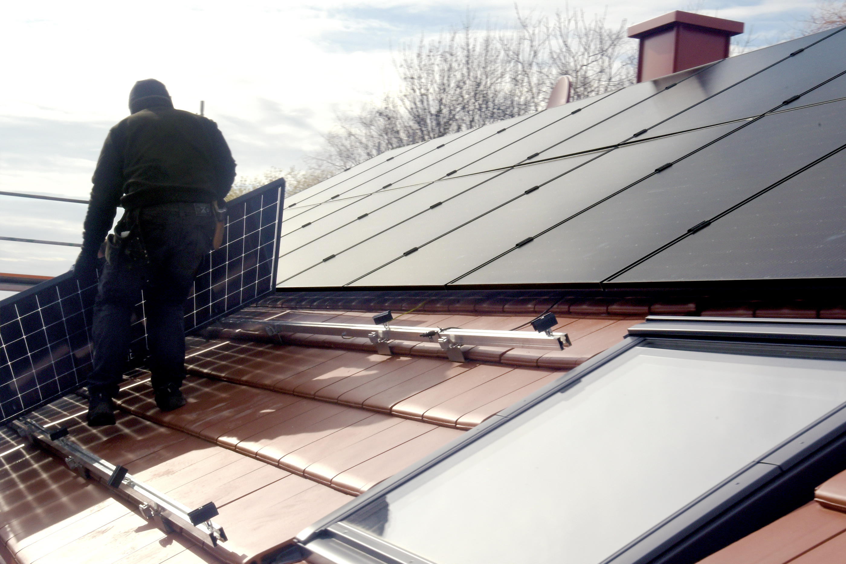 Ein Mann steht auf einem Dach und montiert eine PV Anlage von der NEW Energie zur Herstellung von günstigem Ökostrom.
