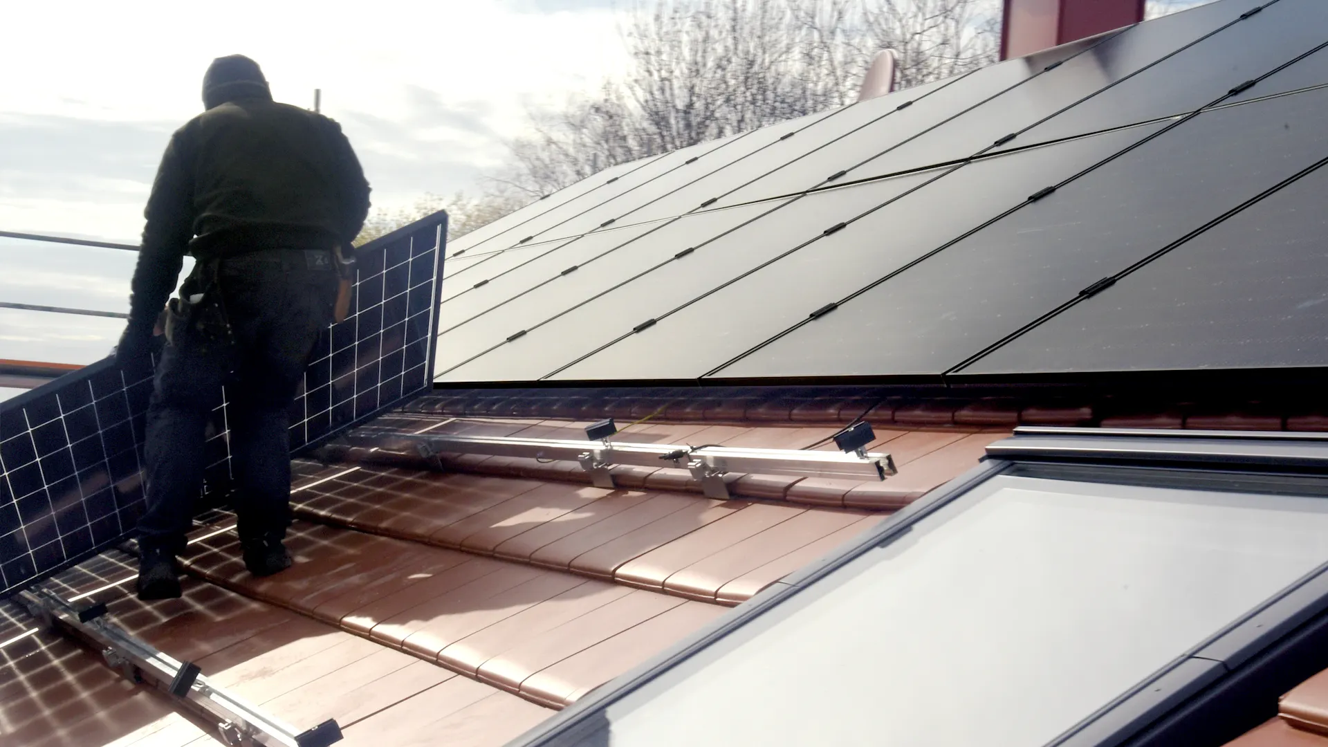 Mann montiert eine Photovoltaikanlage Ein Mann steht auf einem Dach und montiert eine PV Anlage von der NEW Energie zur Herstellung von günstigem Ökostrom.