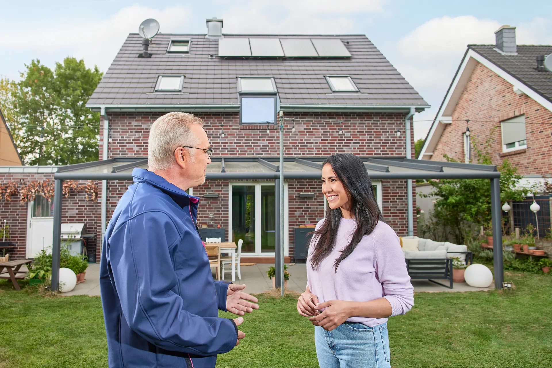 Ein NEW Mitarbeiter berät eine Kundin vor ihrem Einfamilienhaus bezüglich einer Photovoltaikanlage und grüner Energie.