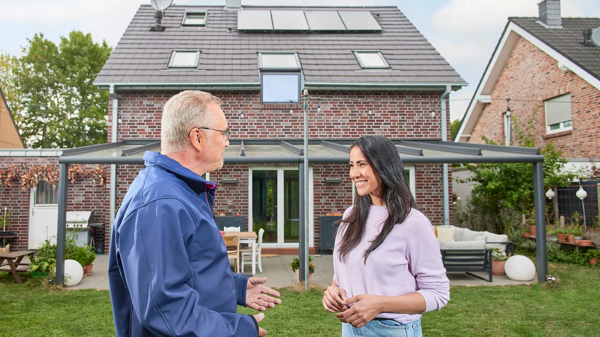 Beratung Photovoltaikanlage Ein NEW Mitarbeiter berät eine Kundin vor ihrem Einfamilienhaus bezüglich einer Photovoltaikanlage von der NEW Energie und grüner Energie.