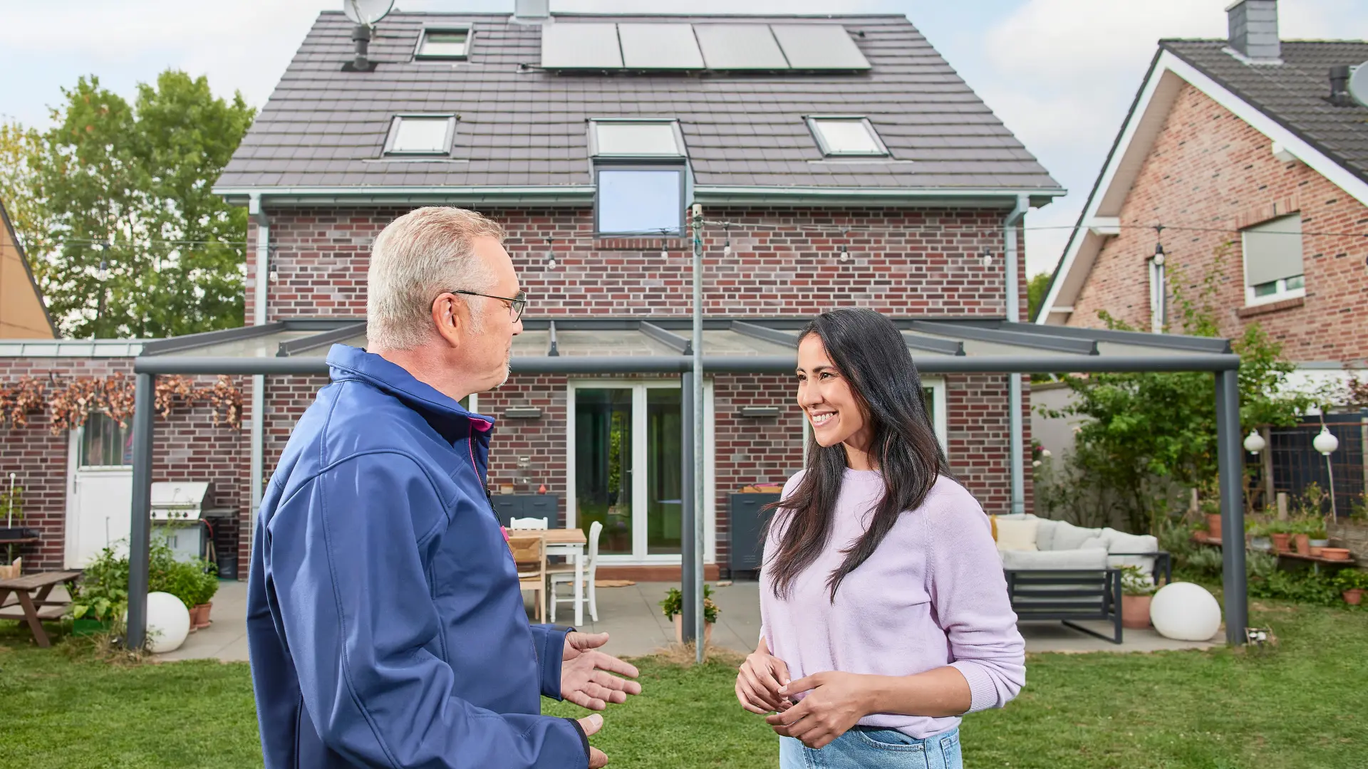 Ein NEW Mitarbeiter berät eine Kundin vor ihrem Einfamilienhaus bezüglich einer Photovoltaikanlage und grüner Energie.