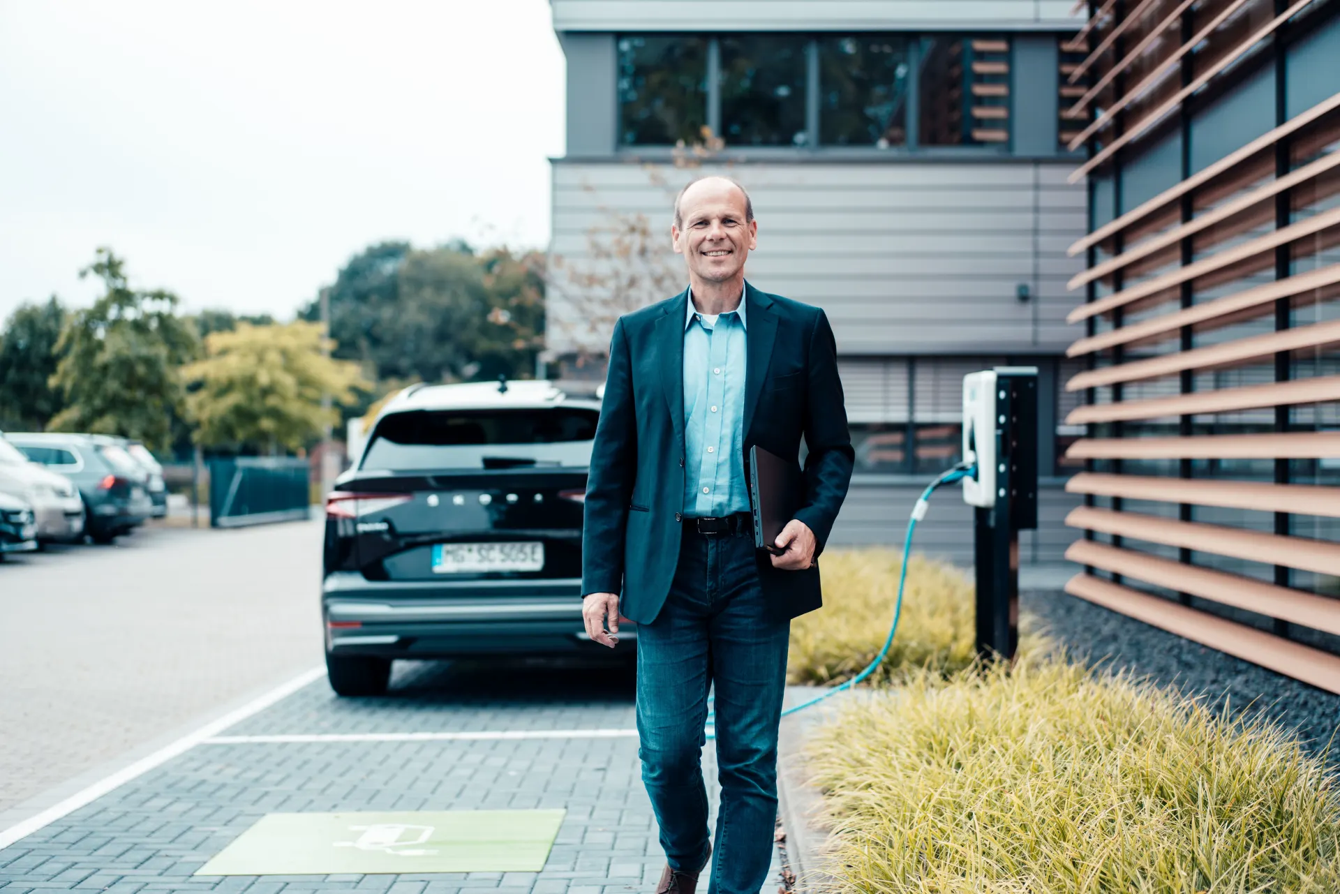 Unternehmer geht von seinem E-Auto weg, was mit Hilfe einer Wallbox auflädt.