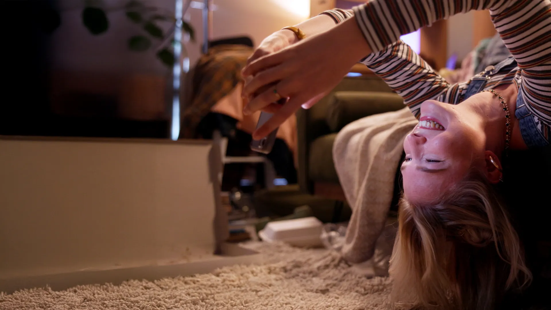 Entspannen können mit dem ausgezeichneten Service der NEW Energie Frau liegt kopfüber von ihrem Sofa und schaut lachend auf ihr Smartphone.