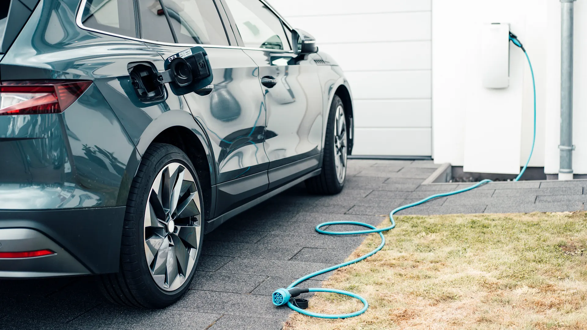 Ladestecker in der Wallbox Ein Ladekabel hängt in einer Wallbox der NEW Energie. Ein E-Auto steht daneben.