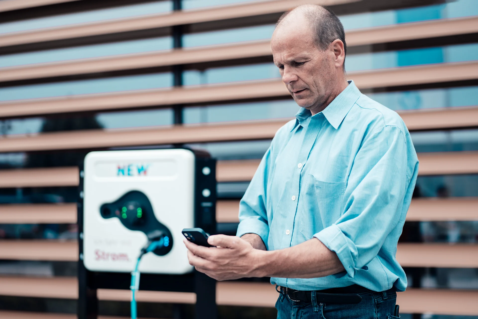 Ein Mann schaut auf sein Handy vor einer Ladestation für Elektromobilität.