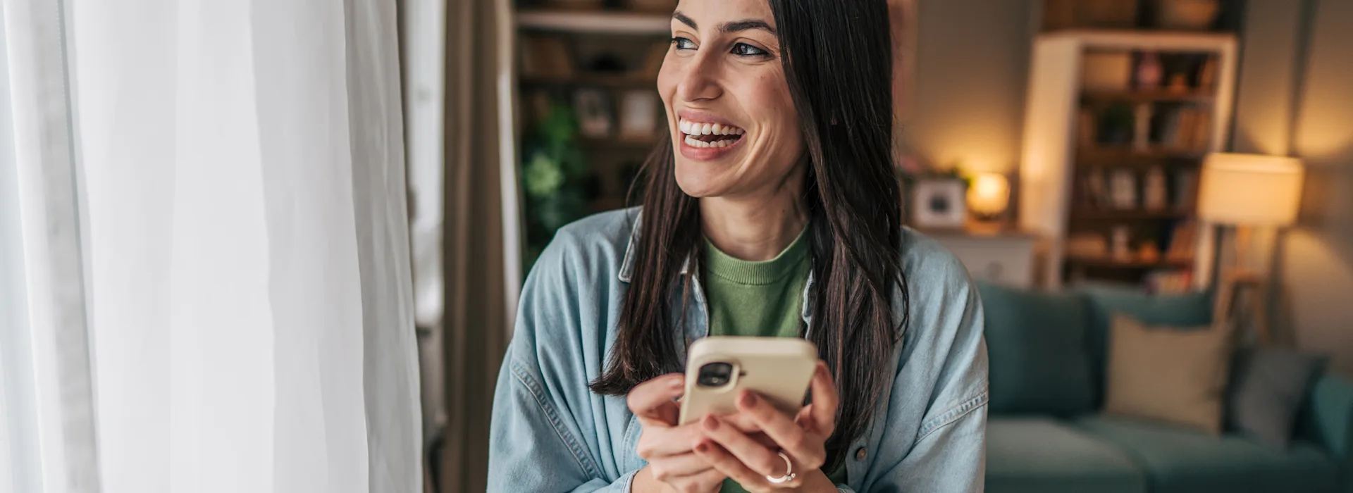 Frau am Fenster schaut NEW Energie Tarife Eien Frau steht am Fenster und schaut auf ihrem Smartphone die günstigen Tarife der NEW Energie an.