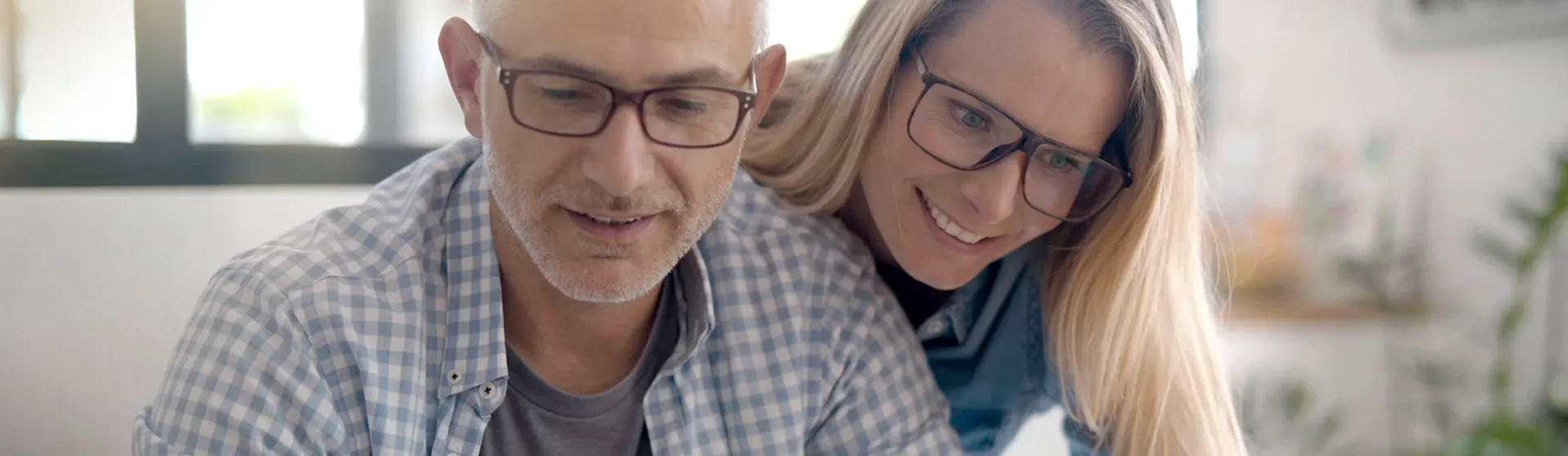 Pärchen informiert sich über die Services der NEW Energie Eine Frau schaut ihrem Mann über die Schulter. Er arbeitet am Laptop und besucht die Seite von der NEW Energie.