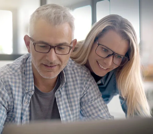 Pärchen informiert sich über die Services der NEW Energie Eine Frau schaut ihrem Mann über die Schulter. Er arbeitet am Laptop und besucht die Seite von der NEW Energie.