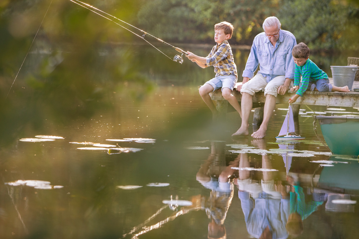 Ein Mann sitzt mit zwei kleinen Kindern an einem See und angelt.