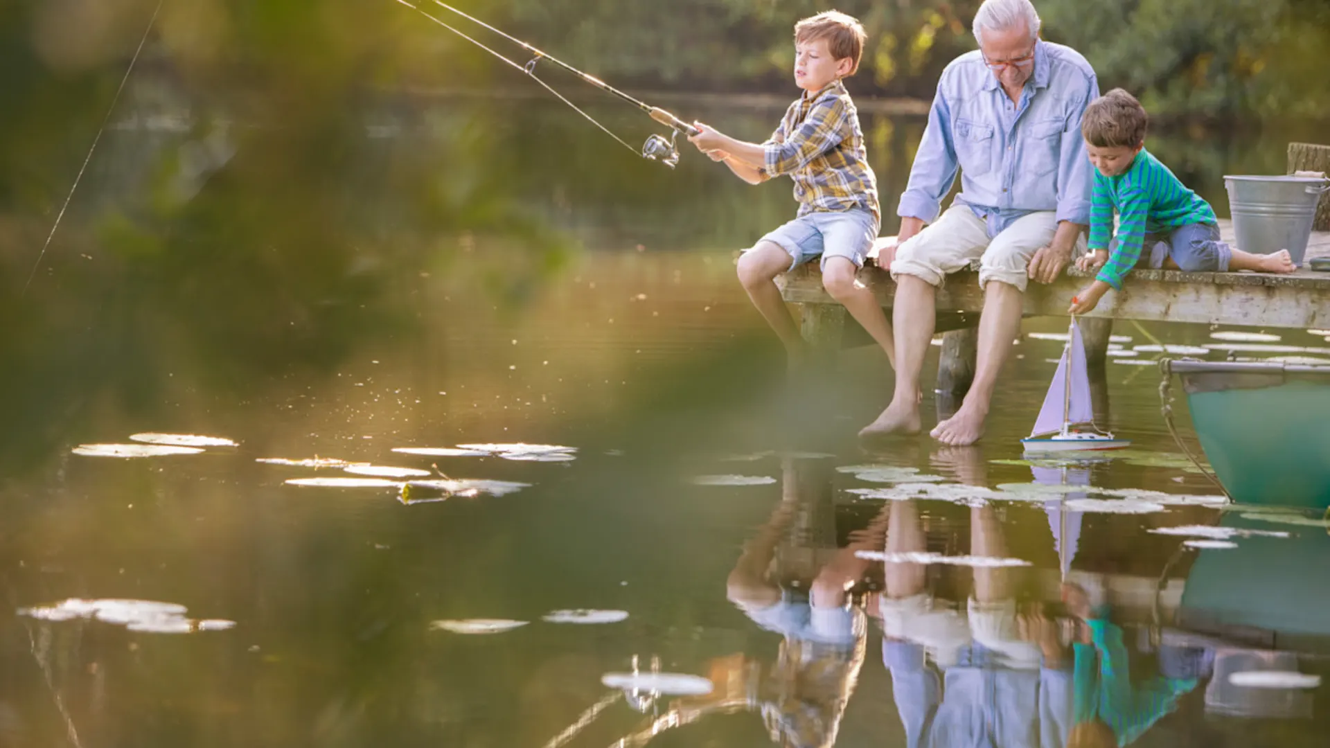 Smart City GmbH Ein Mann sitzt mit zwei kleinen Kindern an einem See und angelt.