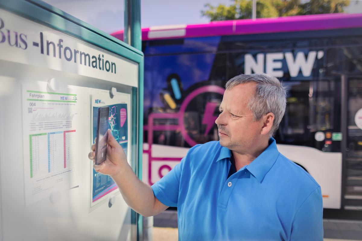 Fahrgast steht an Bushaltestelle und scannt mit seinem Smartphone ein QR-Code ein.