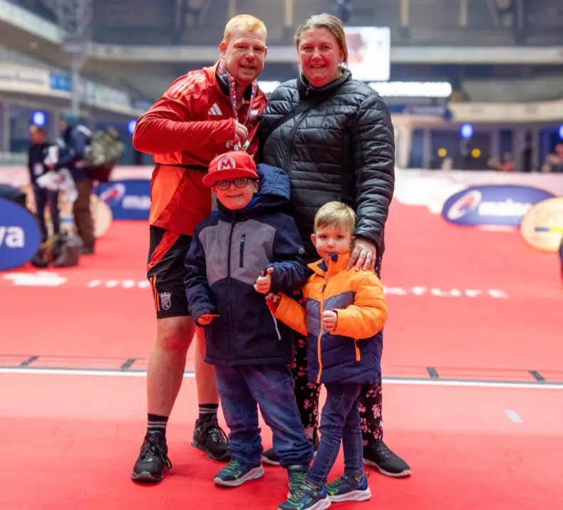 Martin Giesers-Aviles in roter Sportkleidung steht mit seiner Frau Manuela und den beiden Söhnen Lukas und Christian lächelnd im Zielbereich einer Laufveranstaltung in einem Stadion.