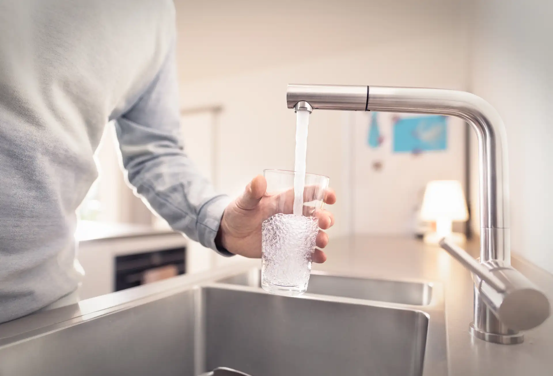 Eine Person steht vor einem Spülbecken und füllt ein Glas mit Wasser