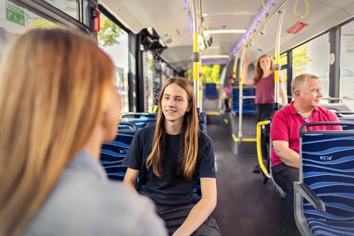 Verschiedene Personen aller Altersgruppen sitzend in einem NEW Bus.