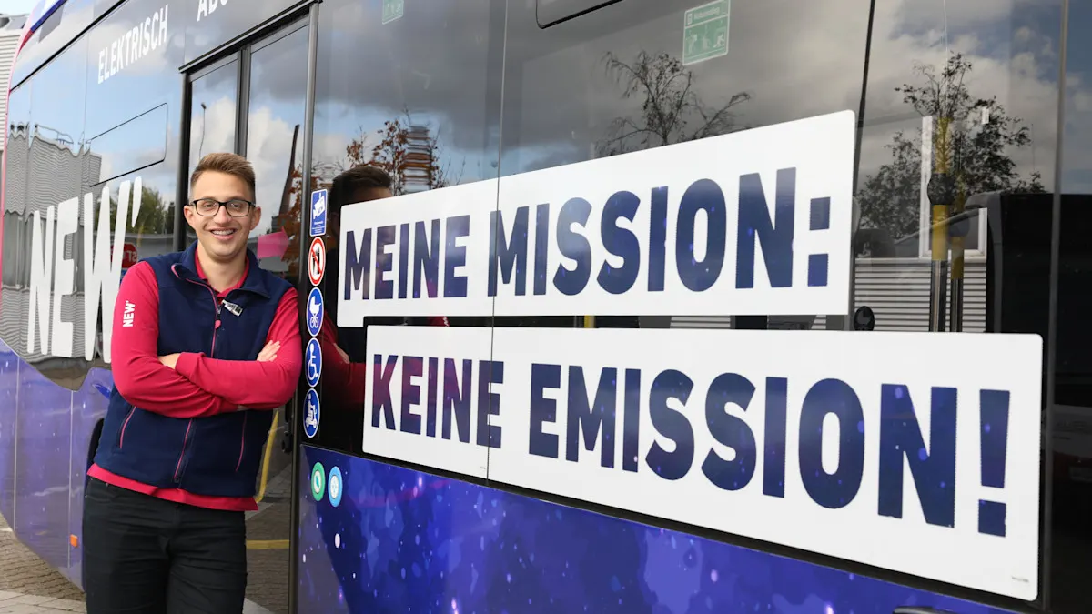 NEW Mitarbeiter steht angelehnt an einem neuen NEW E-Bus neben dem großen Aufkleber "Meine Mission: Keine Emission!"