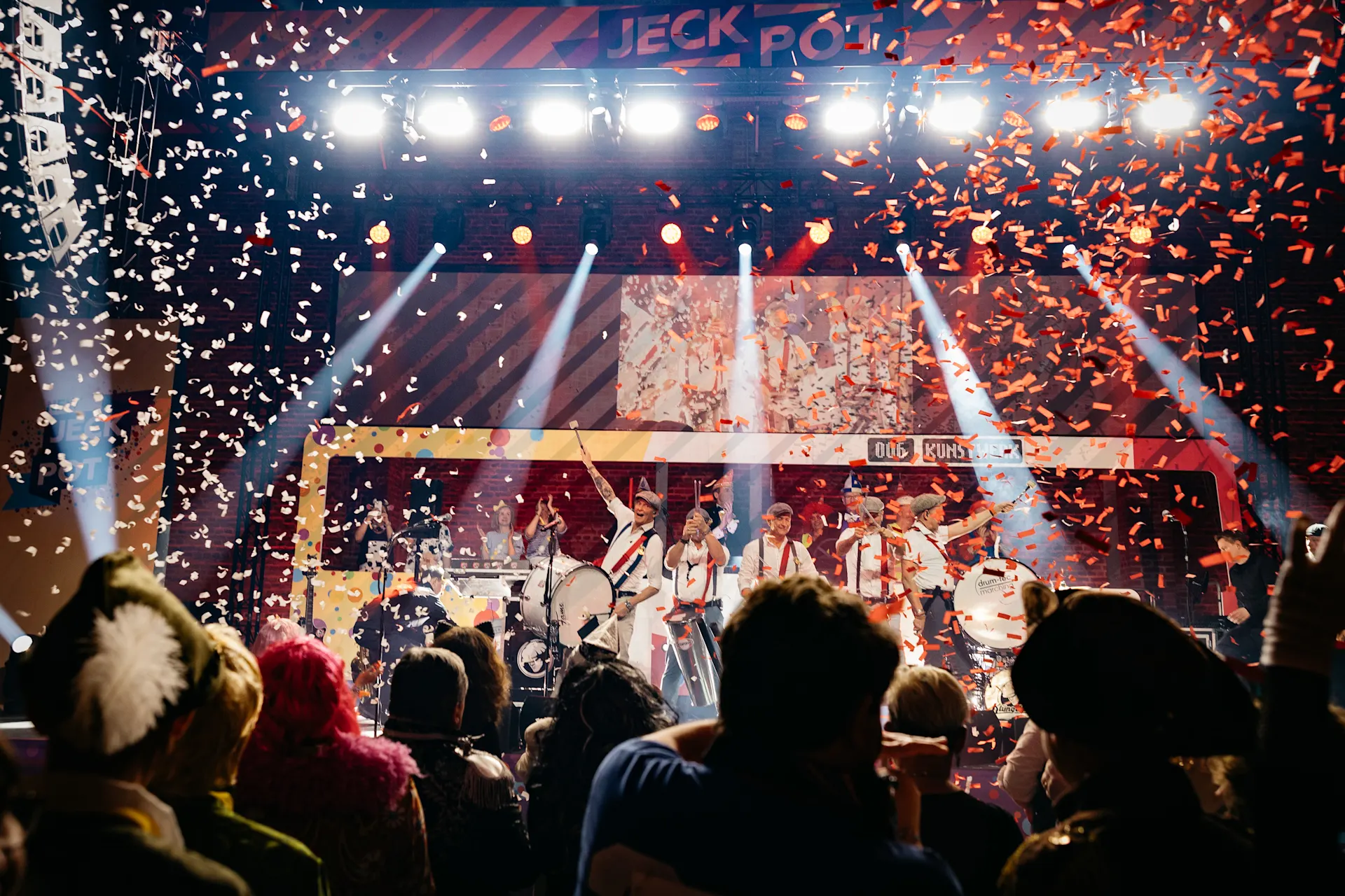 Bühnenshow mit Band vor jubelndem Publikum, während Konfetti von der Decke regnet. Bühnenschrift 'JECK POT' ist sichtbar, bunte Beleuchtung und Scheinwerfer tauchen die Szenerie in spektakuläres Licht.  Credit: Felix Küster