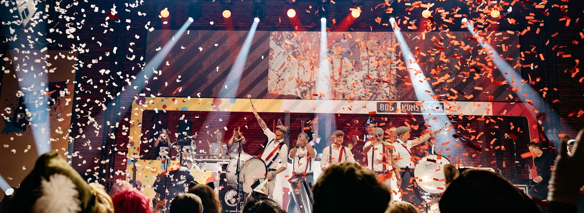 Jeck Pot 2025 - Impressionen Bühnenshow mit Band vor jubelndem Publikum, während Konfetti von der Decke regnet. Bühnenschrift 'JECK POT' ist sichtbar, bunte Beleuchtung und Scheinwerfer tauchen die Szenerie in spektakuläres Licht. Credit: Felix Küster
