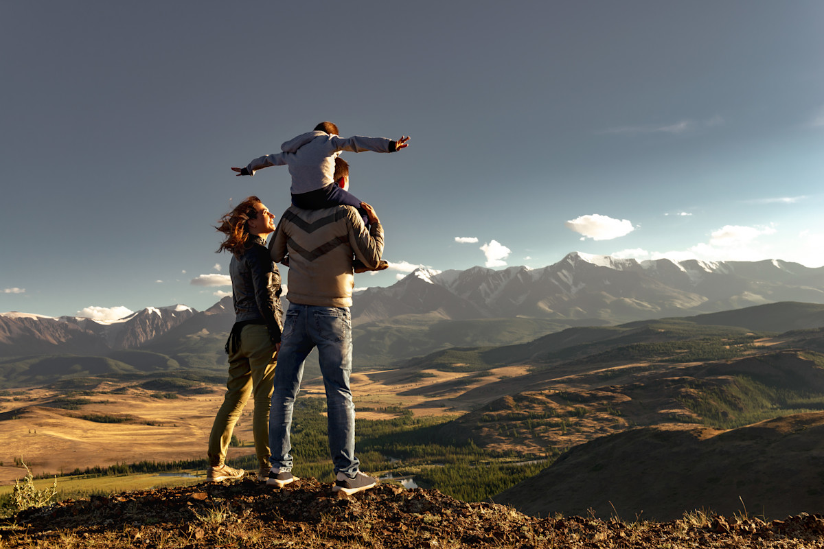 Eine Familie steht auf einer hügeligen Landschaft mit Blick auf ein paar Berge.