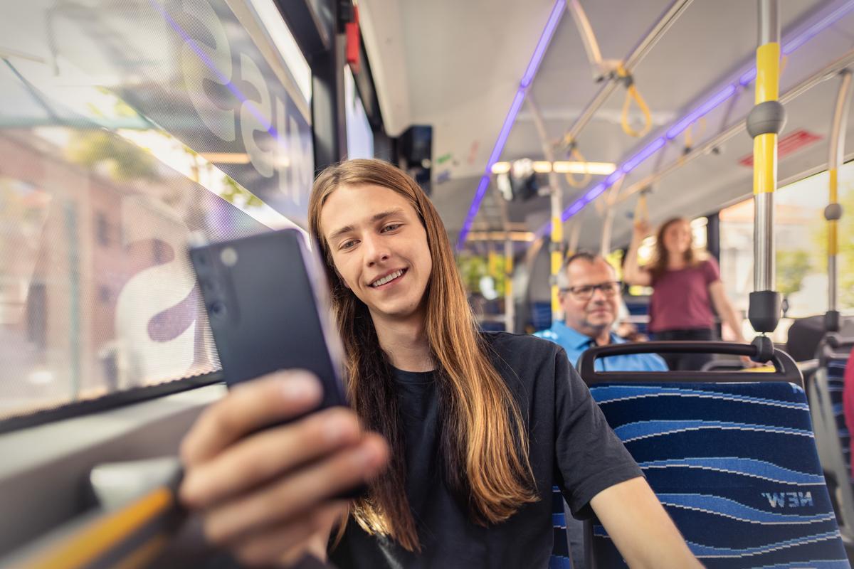 Junger Mann sitzt im Bus und schaut auf sein Smartphone.