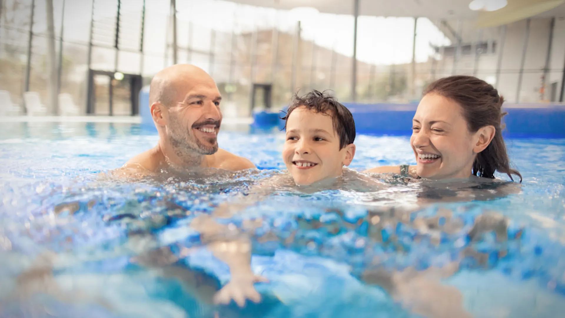 Familienzeit im Schwimmbad Ein lächelndes Ehepaar mit ihrem Kind im Freizeitbecken eines Schwimmbades