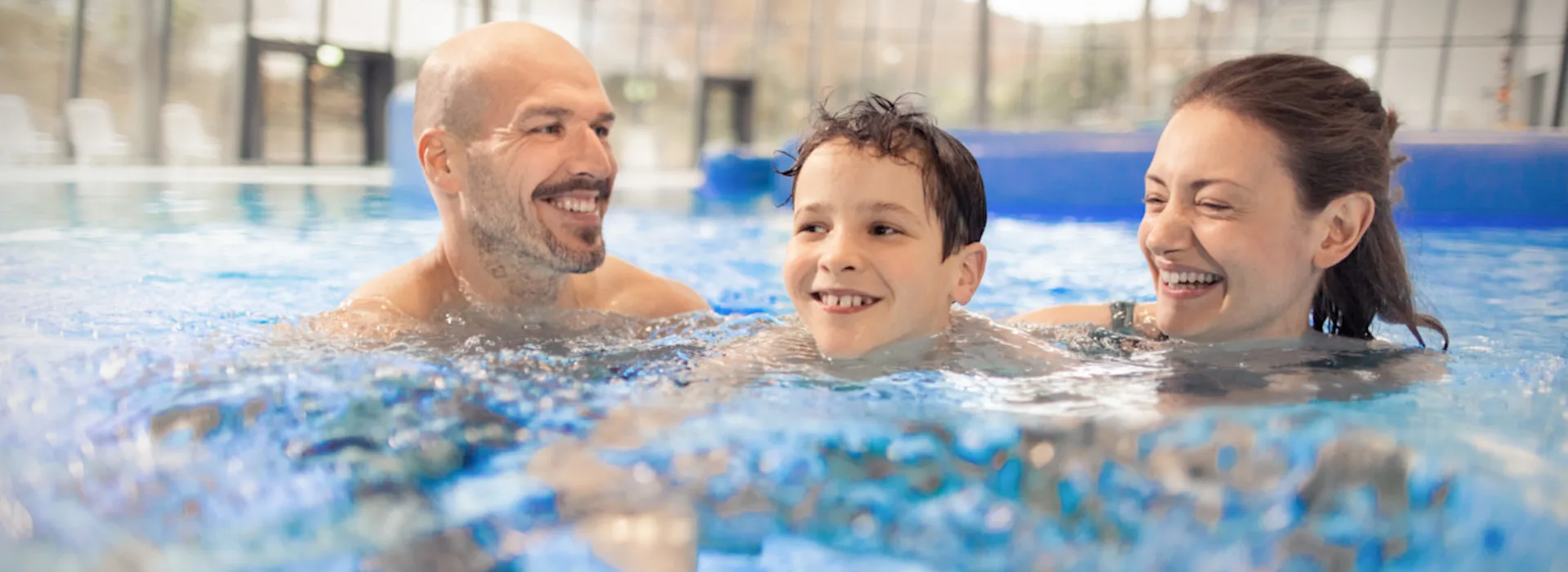 Familienzeit im Schwimmbad Ein lächelndes Ehepaar mit ihrem Kind im Freizeitbecken eines Schwimmbades