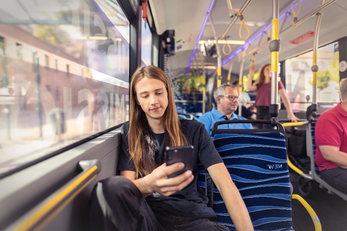 Junger Mann sitzt im Bus und schaut auf sein Smartphone.