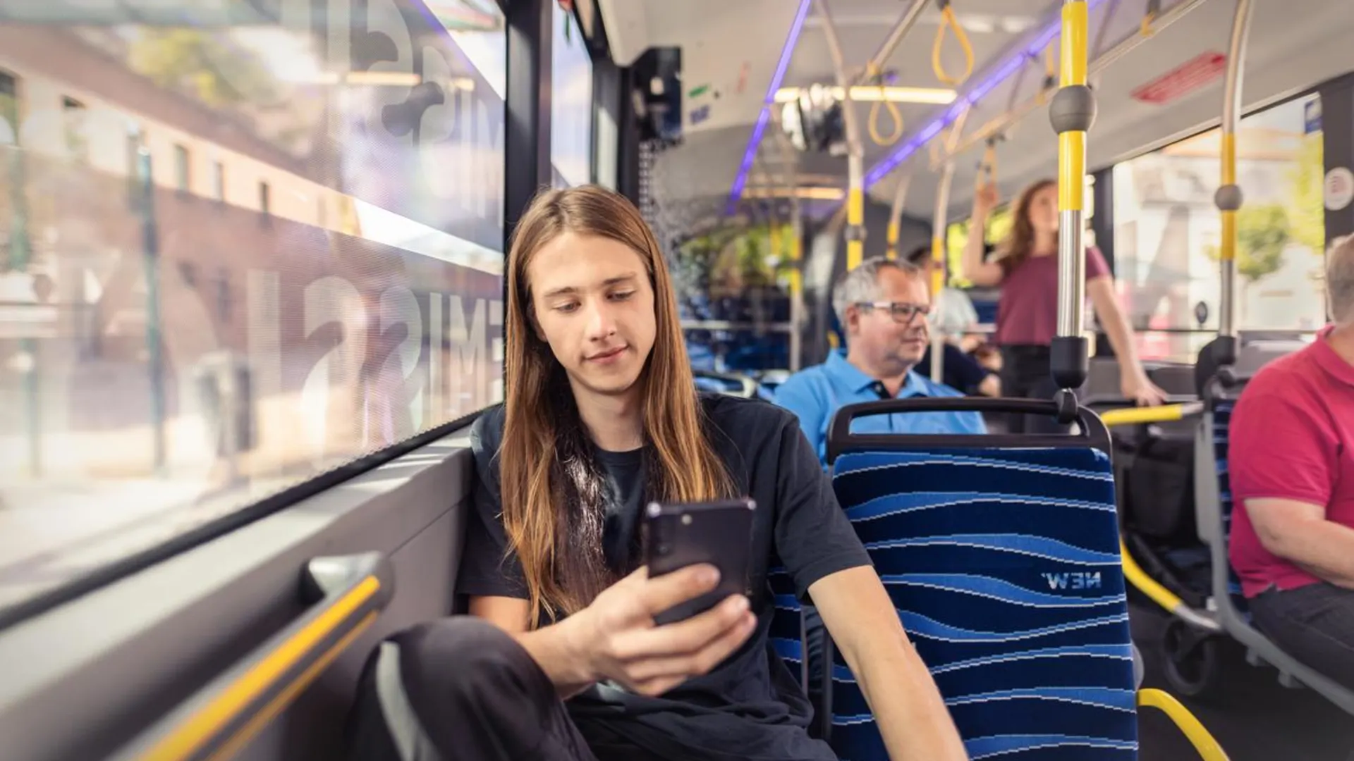 Tickets und Tarife Junger Mann sitzt im Bus und schaut auf sein Smartphone.