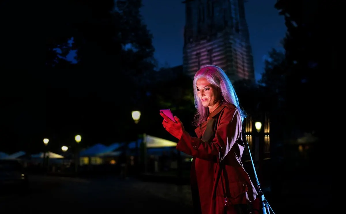 Frau ist abends draußen unterwegs und schaut in ihr Smartphone.