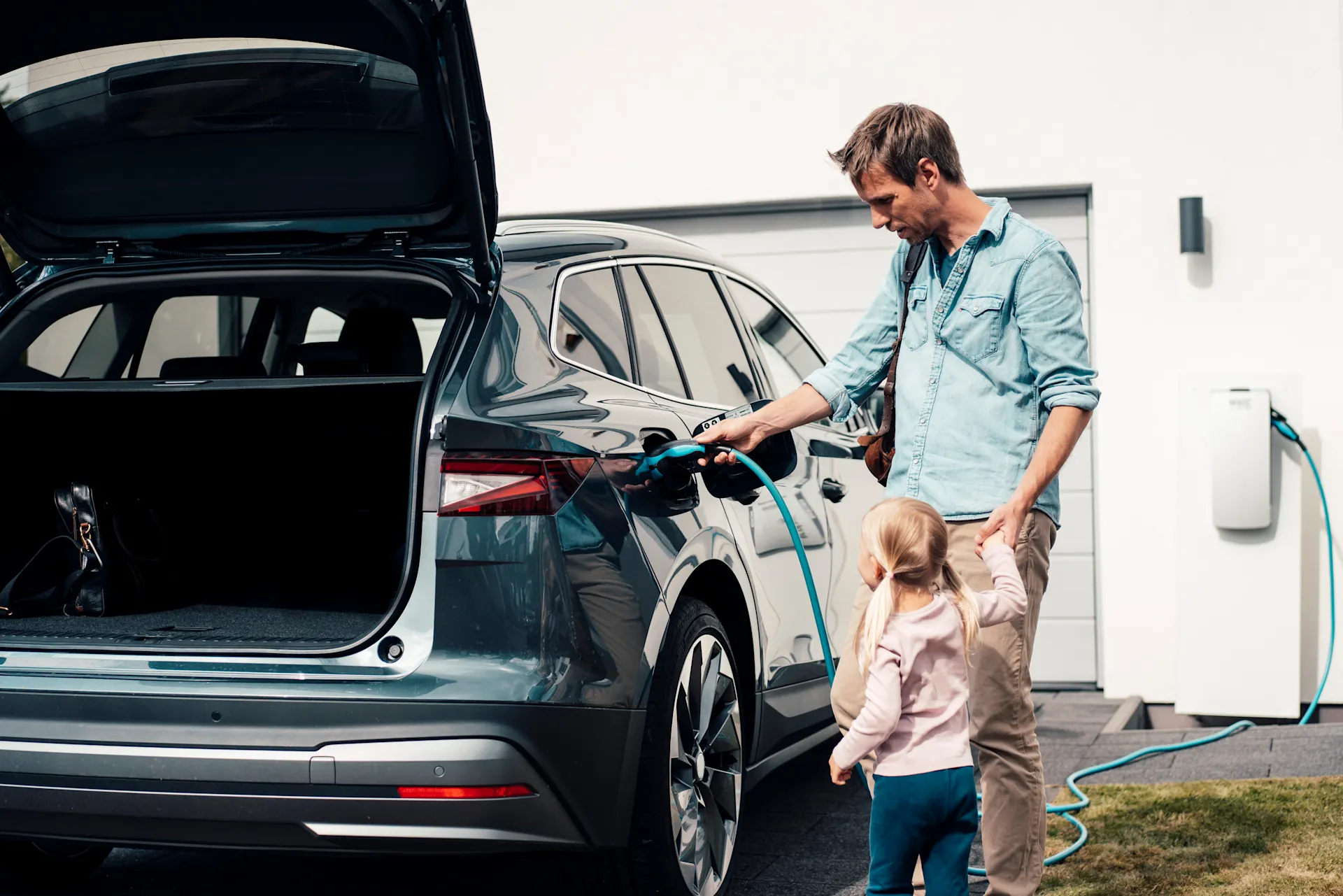 Vater und Tochter stehen am ladenden E-Auto.