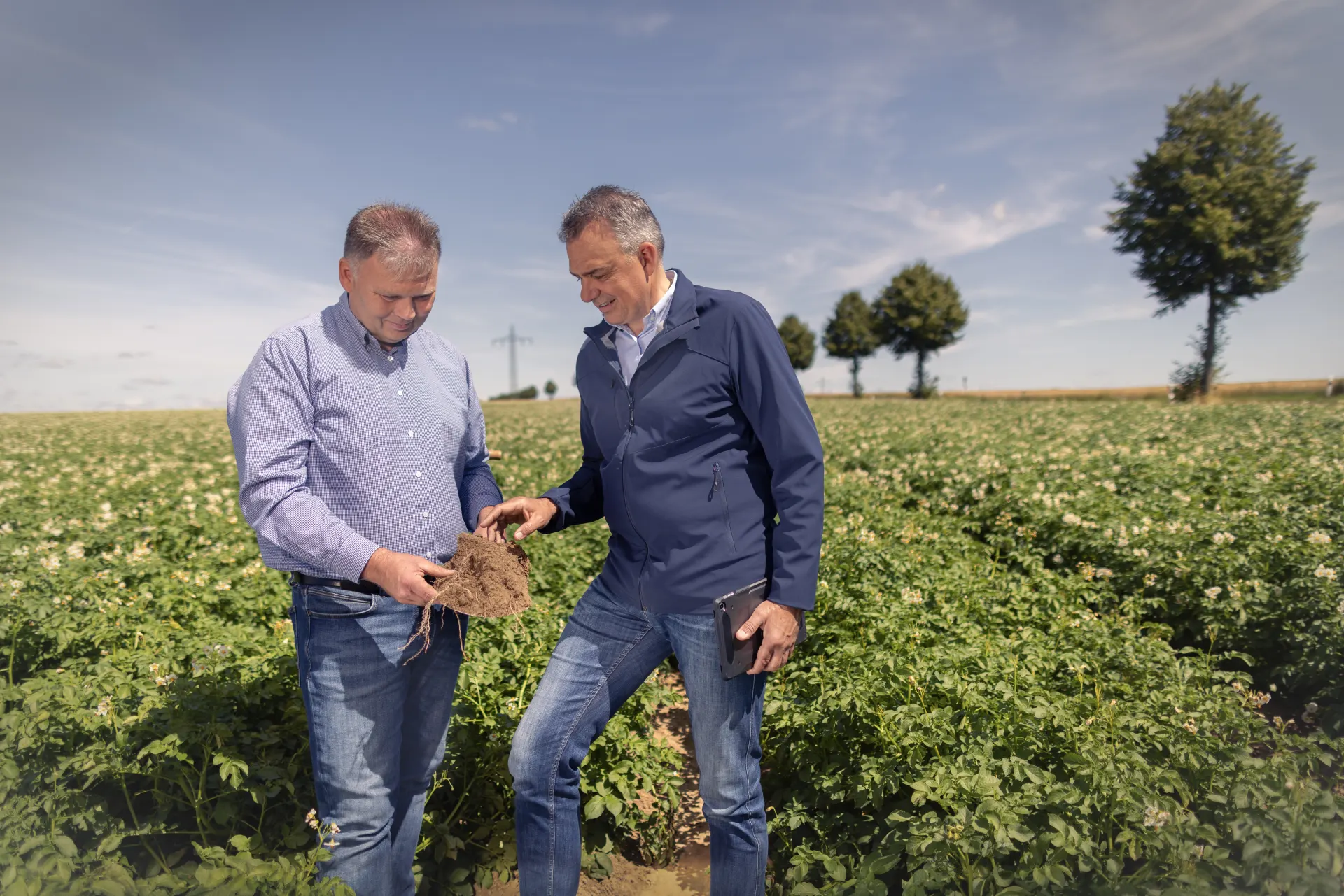 Ein Mitarbeiter und ein Landwirt untersuchen die Bodenqualität auf einem Feld