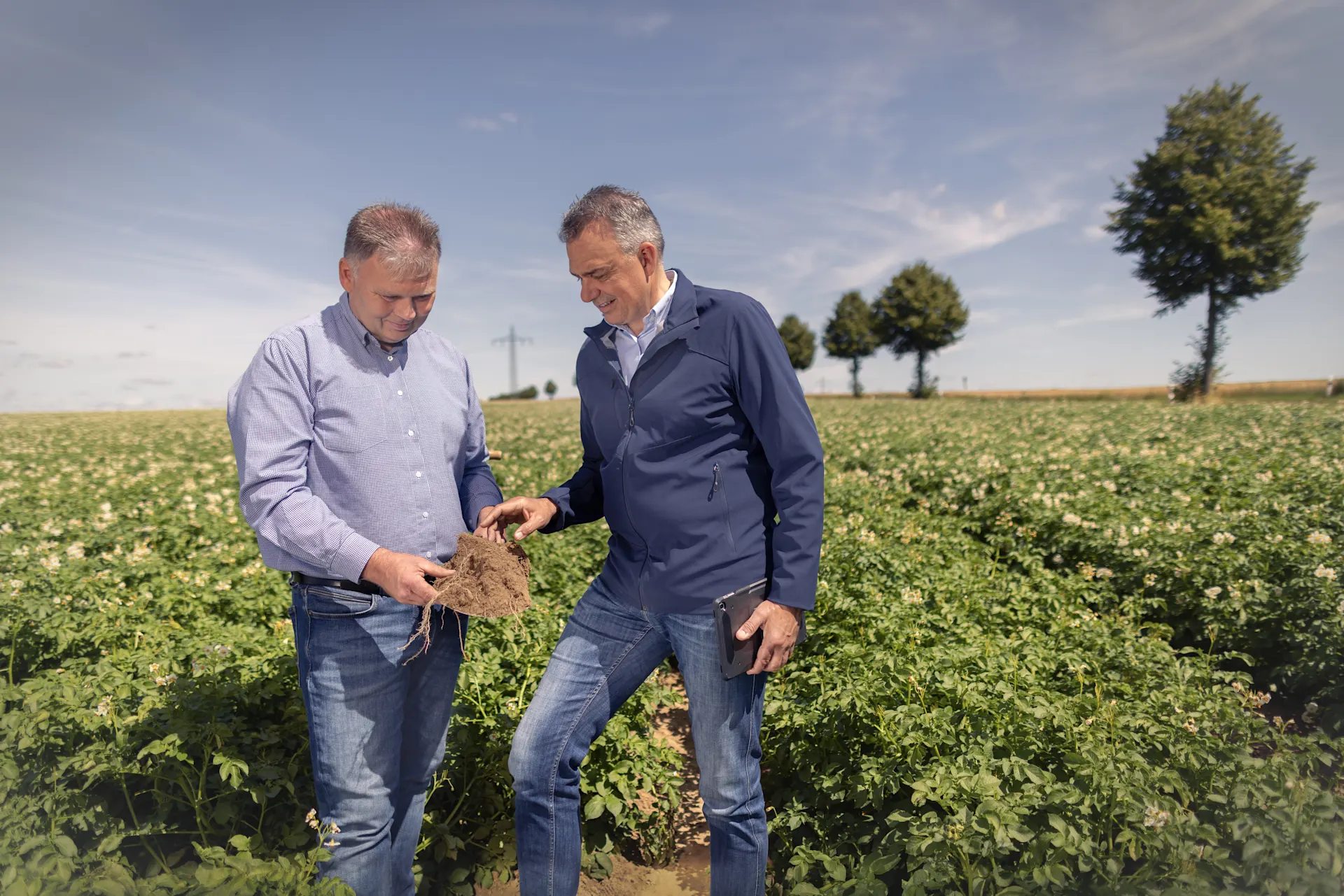 Ein Mitarbeiter und ein Landwirt untersuchen die Bodenqualität auf einem Feld