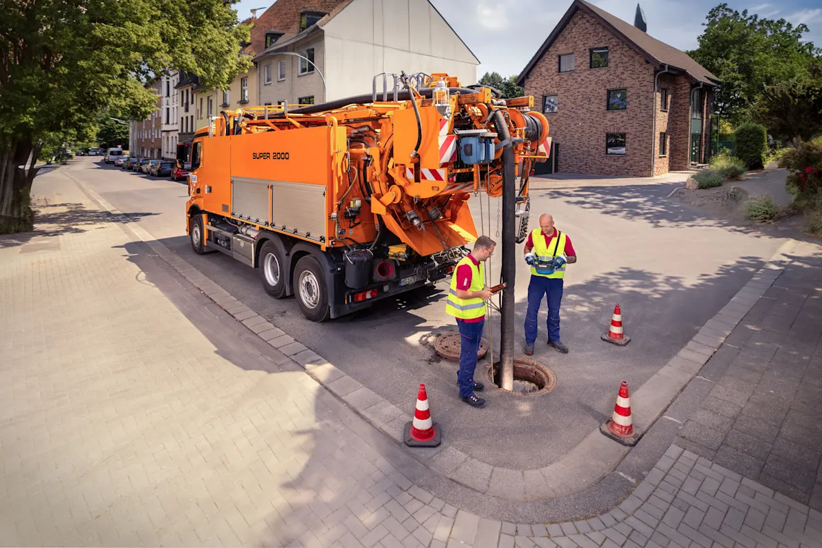 Luftaufnahme eines Saug- und Spülfahrzeuges mit zwei Kollegen an einem Kanalschacht