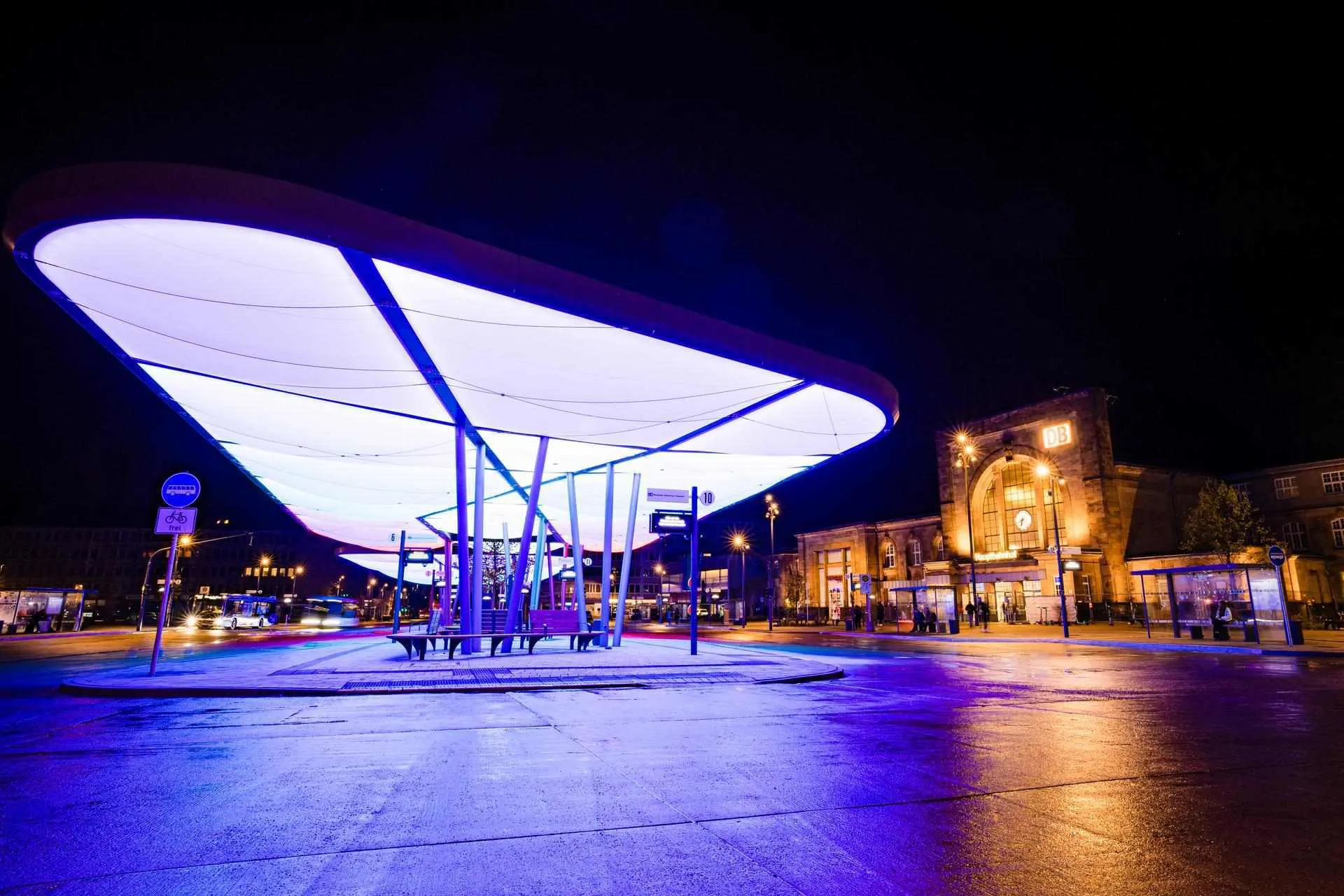 Das Bild zeigt den Zentralen Omnibusbahnhof (ZOB) in Mönchengladbach bei Nacht. Die moderne Dachkonstruktion ist beleuchtet und prägt das Stadtbild. Im Hintergrund (rechts) befindet sich der Hauptbahnhof