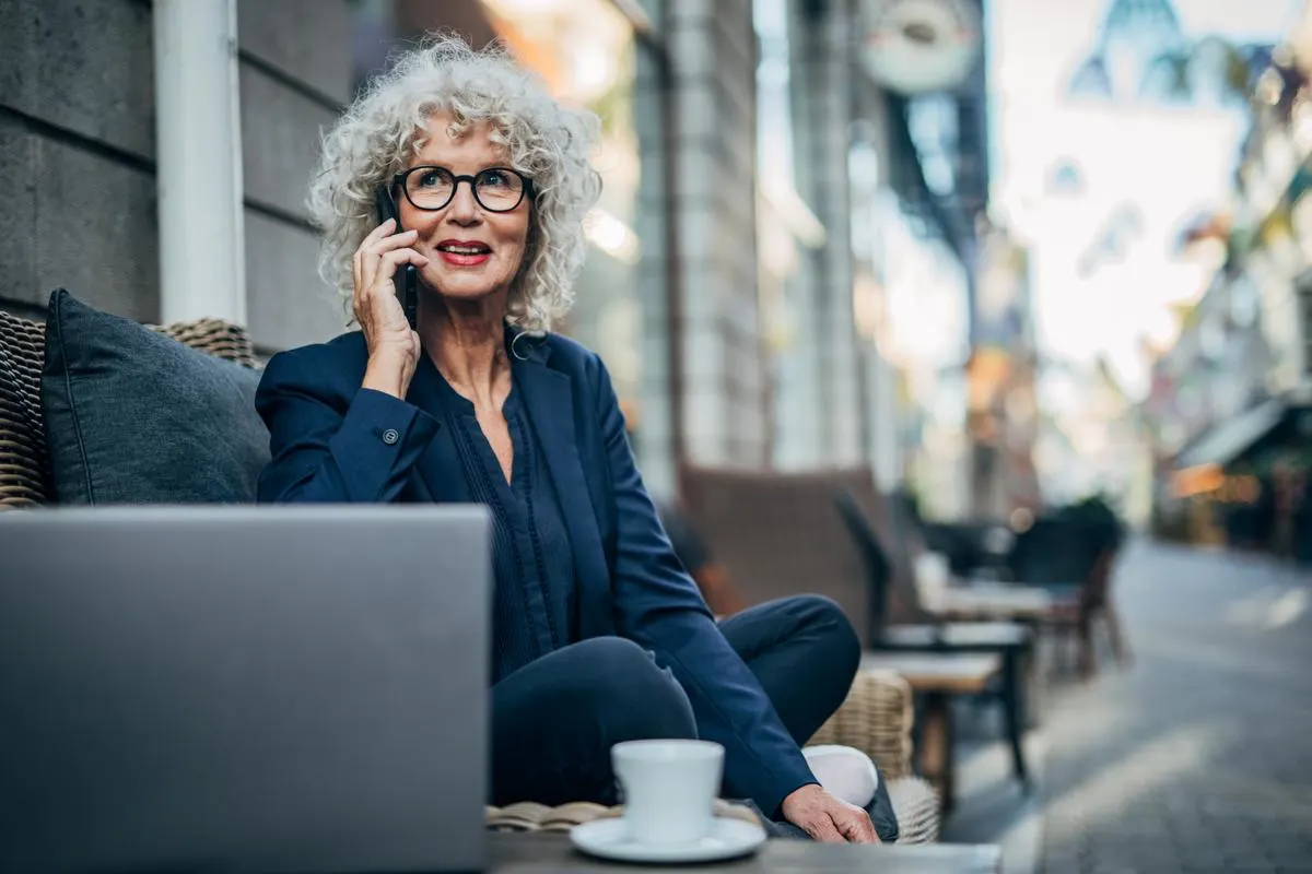 Frau die im Café an einem Laptop sitzt und telefoniert.