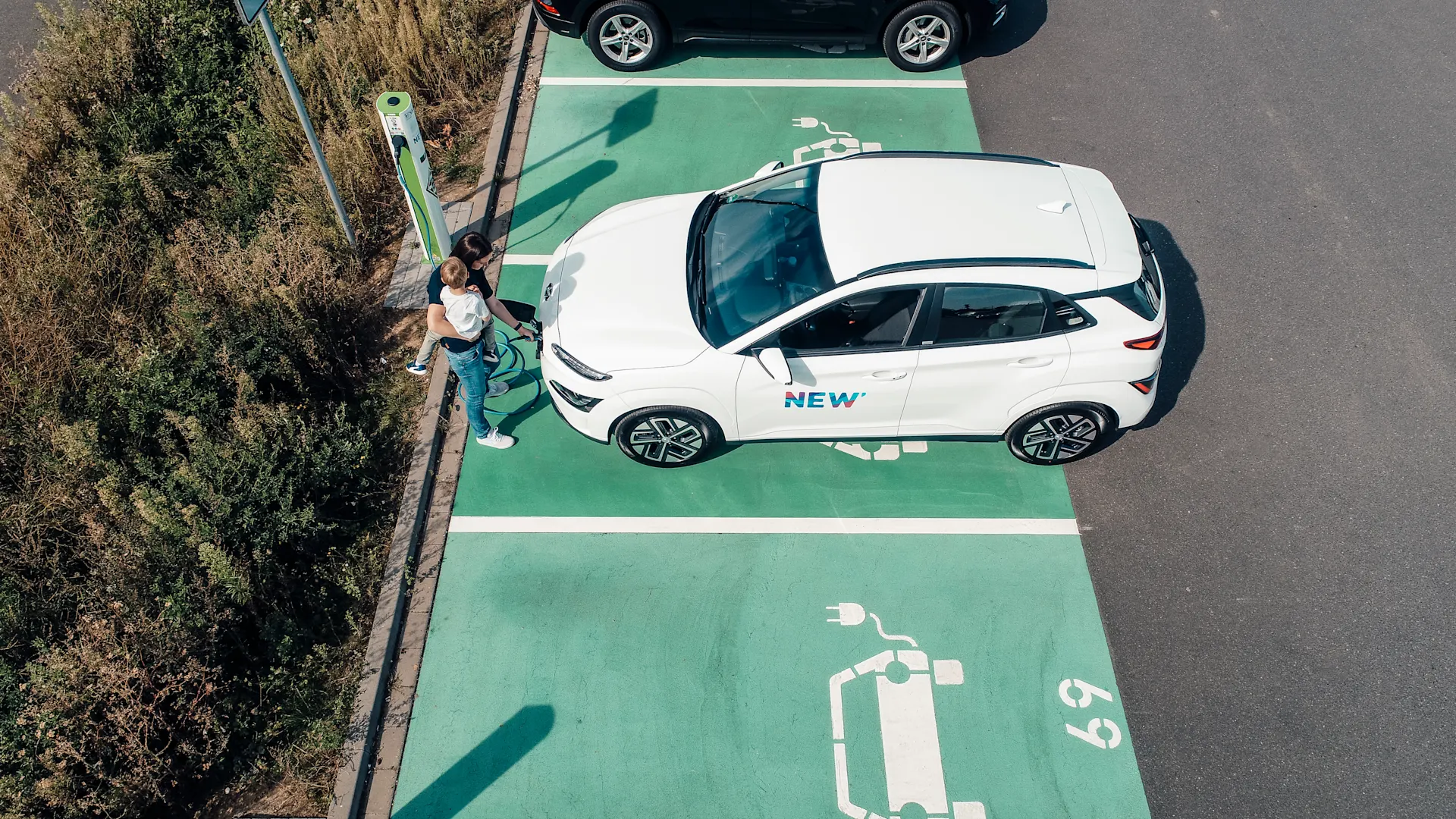 Leichtes E-Laden Frau lädt mit einem Kind auf dem Arm das E-Auto.